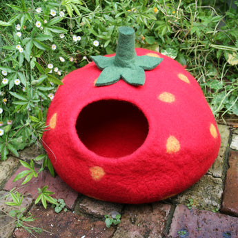 Red strawberry-shaped felt cat cave bed on a brick surface with greenery, a cute and cozy eco-friendly felt cat bed cave, perfect cat cave for large cats and pets.