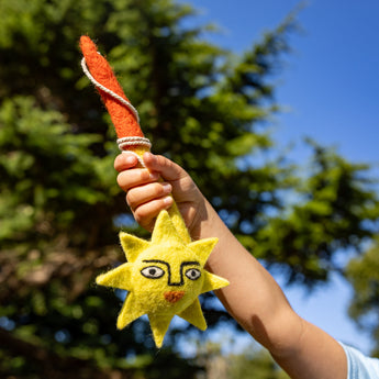 Hand holding a sun-shaped toy with a face against a blurred outdoor background
