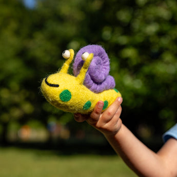 Hand holding a colorful felted snail toy outdoors with greenery in the background