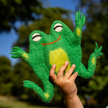 Hand holding a green frog plush toy with a blurred natural background