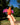 Hand holding a red and pink toy bird against a natural background with trees and blue sky.