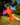 Orange bird-shaped toy with pink wings held in a hand against a blurred outdoor background