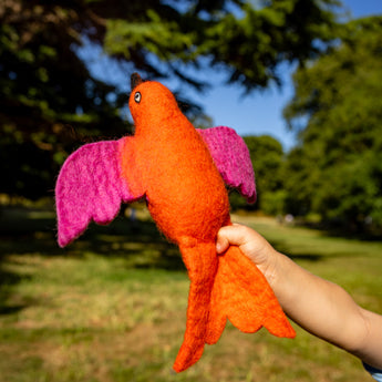 Orange bird-shaped toy with pink wings held in a hand against a blurred outdoor background