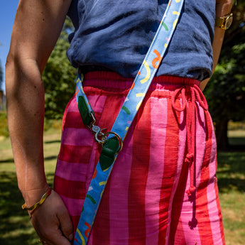 Person wearing a blue shirt and pink plaid pants with a colorful strap over their shoulder outdoors.