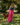 Woman in pink striped pants and blue top standing with a brown dog on a leash in a park.