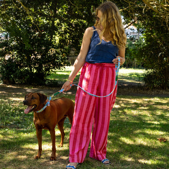 Woman in pink striped pants and blue top standing with a brown dog on a leash in a park.