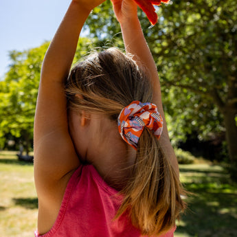 Child holding a red kite in a park with trees and blue sky in the background