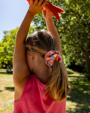 Child holding a red kite in a park with trees and blue sky in the background