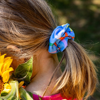 Person with a colorful scrunchie in their hair, surrounded by sunflowers.