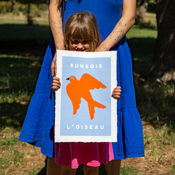 Woman and child holding a poster with an orange bird design outdoors.